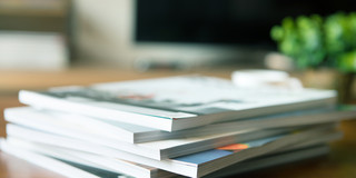 Ein Stapel von Zeitschriften liegt auf einem Holztisch. Es sind sieben Hefte.